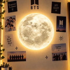 Moon LED wall lamp lit in warm light on a bedroom wall decorated with posters
