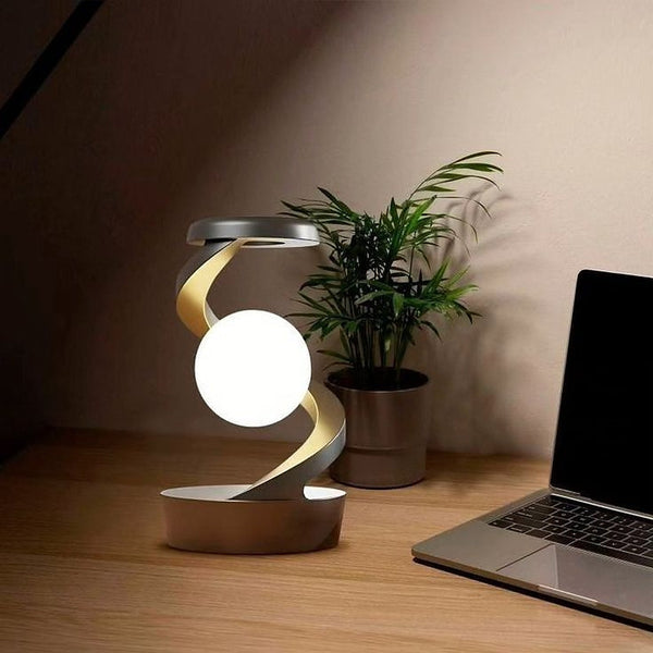 Spiral moon lamp glowing on a wooden desk beside a plant and laptop