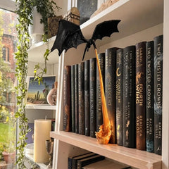 Dragon lamp on a bookshelf, flame base resting beside a row of books